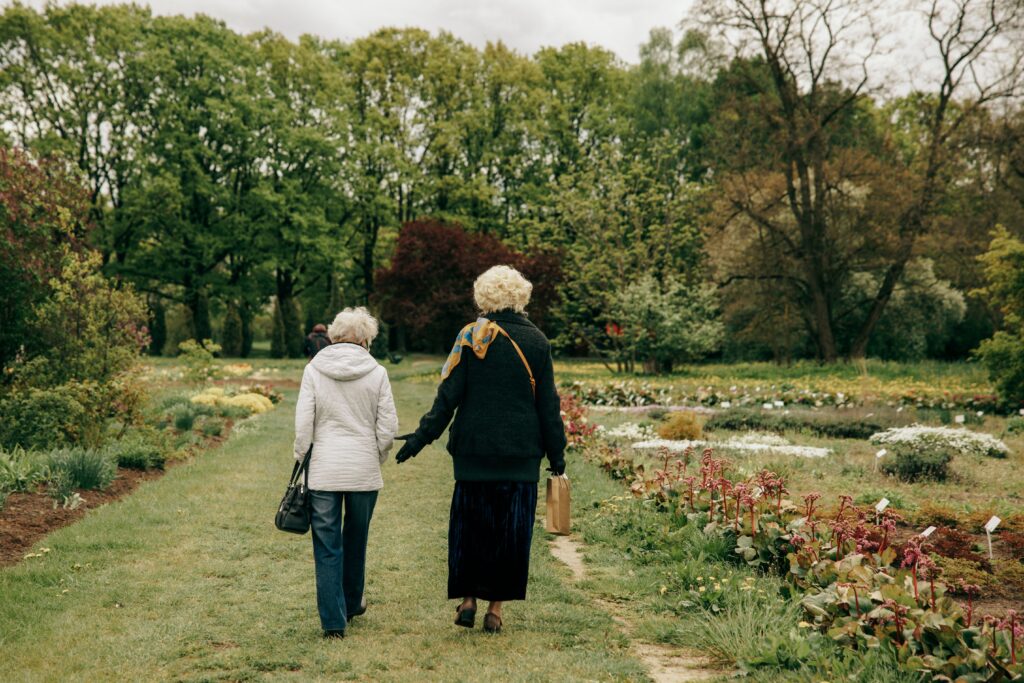 Two older women strolling together along a shaded park path