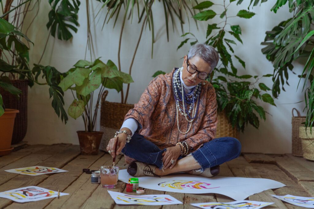 Older woman painting with watercolours at a table surrounded by houseplants
